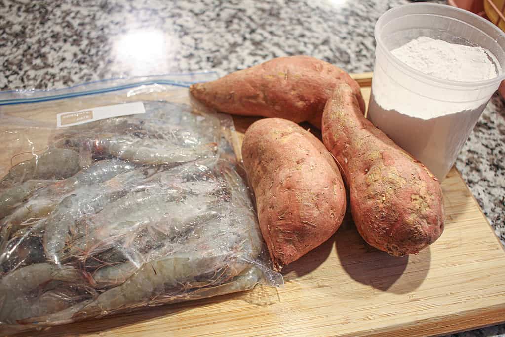 sweet potatoes and a gallon bag of shrimp on a wooden cutting board