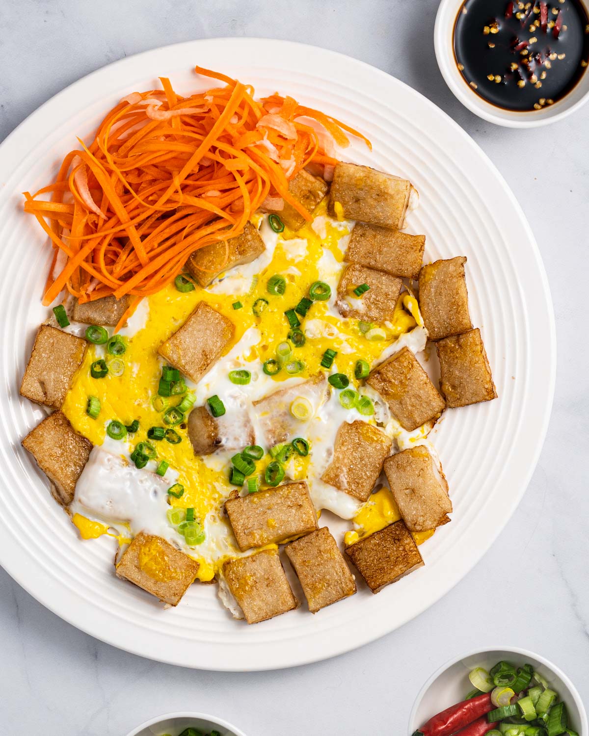 Plate of bot chien (Vietnamese fried rice cakes) with sides of pickled carrots and daikon, dipping sauce, chopped scallions, and red peppers.