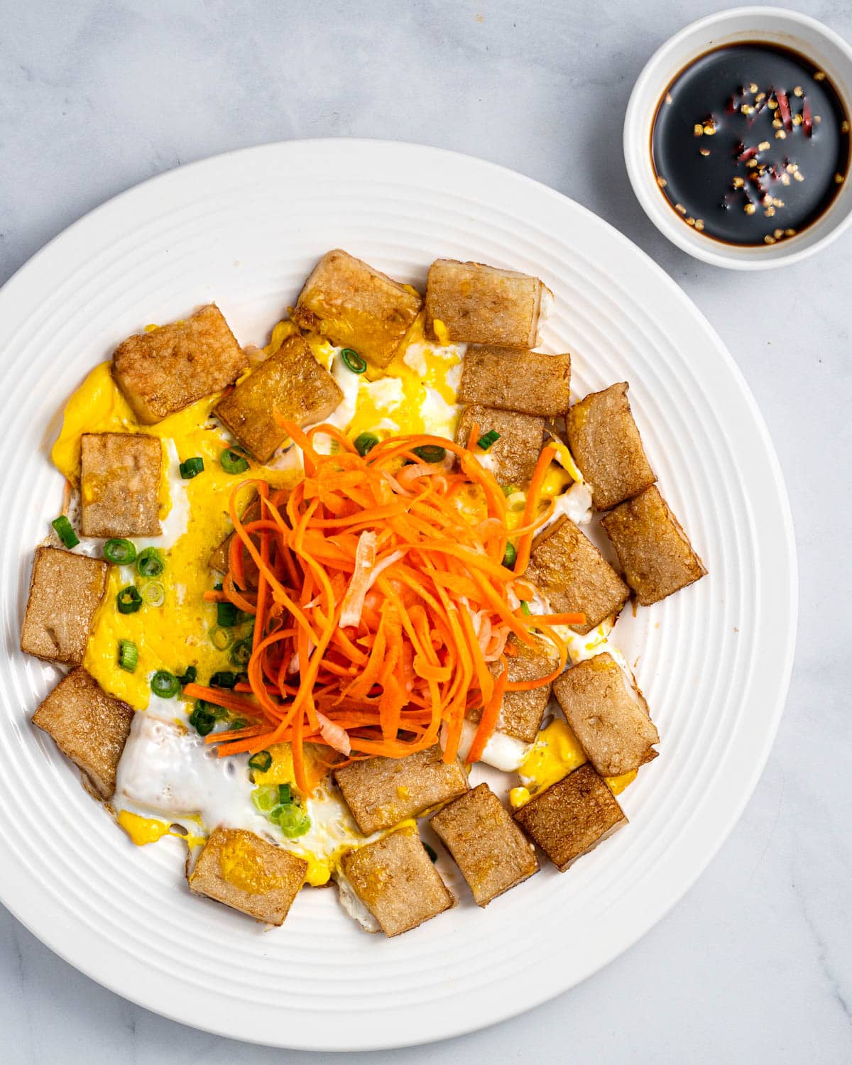 A plate of bot chien with pickled carrots and daikon on top and dipping sauce on the side.