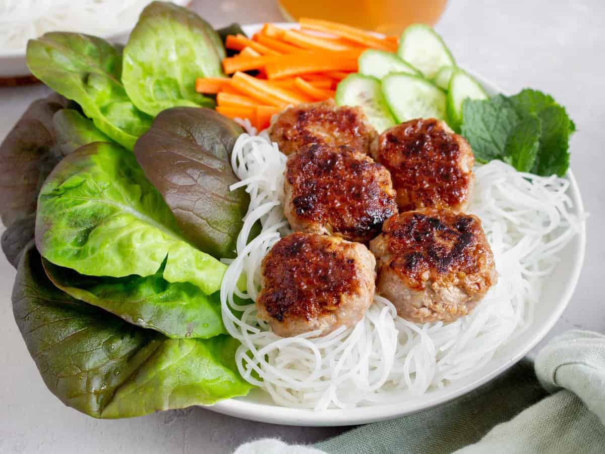 Close up side view of Bún chả in a bowl with rice noodles and vegetables.