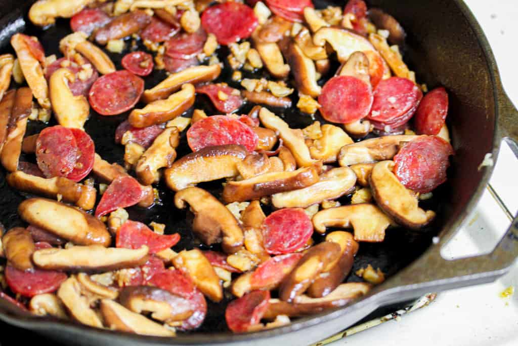 sliced shiitake mushroom, chinese sausage and garlic in a cast iron skillet