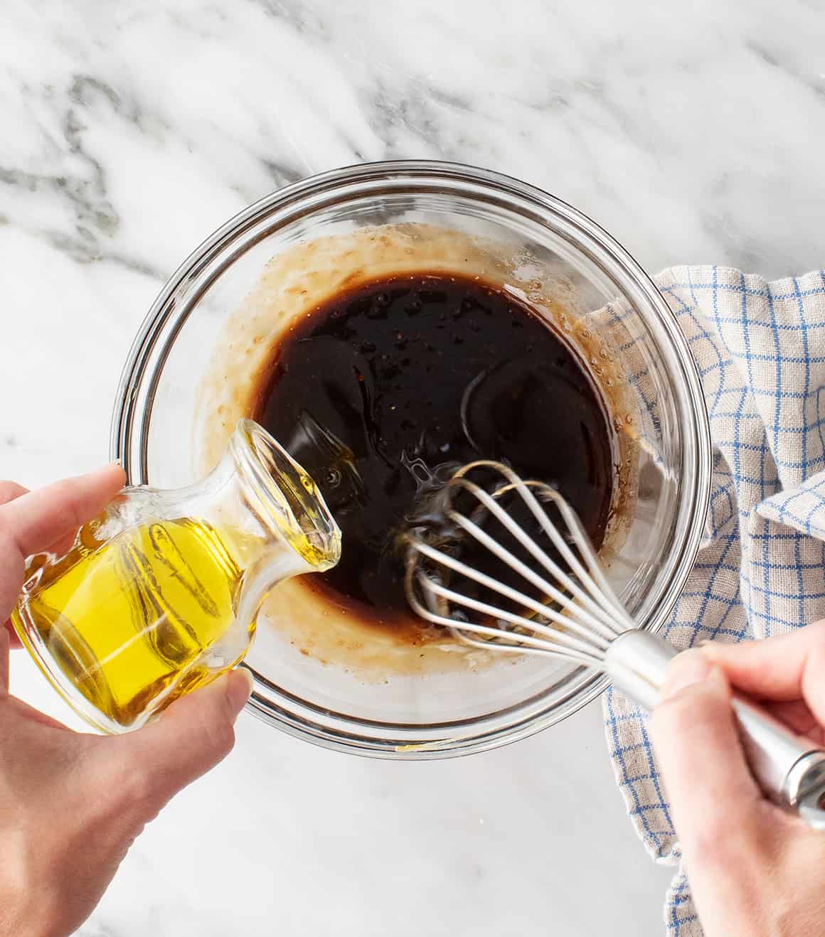 Whisking vinegar in small bowl while pouring in olive oil