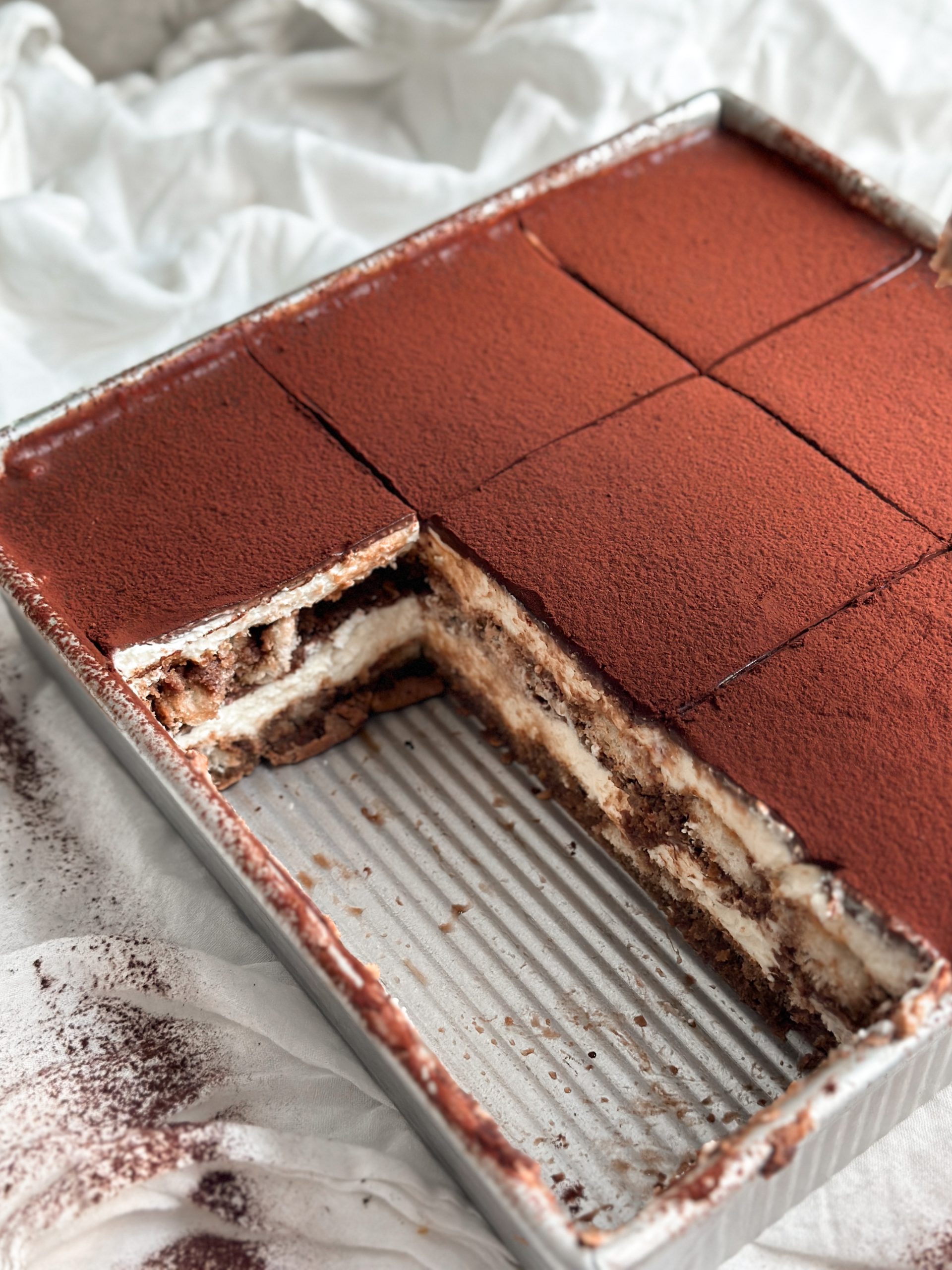 chocolate tiramisu in a serving dish with slices taken out revealing the layers inside from an angle