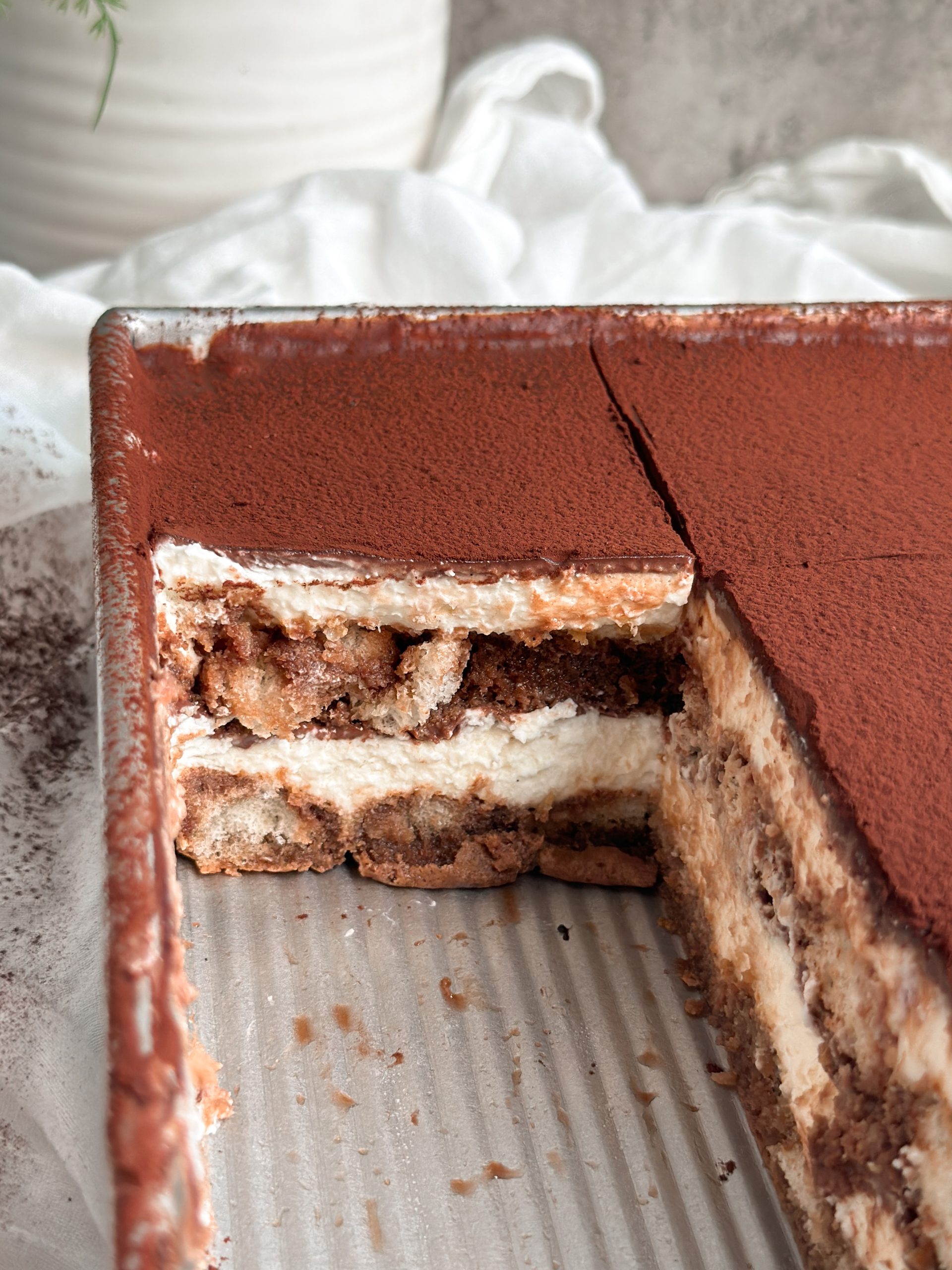 chocolate tiramisu in a serving dish with slices taken out revealing the layers inside