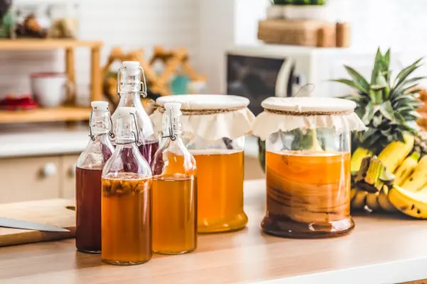 Những chai và hũ đựng kombucha trên bàn bếp, cạnh hoa quả.